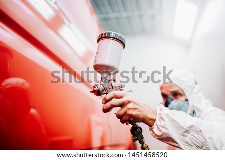 close up of worker painting a red car in a special garage, wearing a white costume