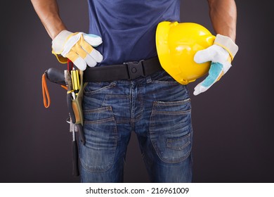 Close Up Of A Worker With Toolbelt And Helmet Against Black Background