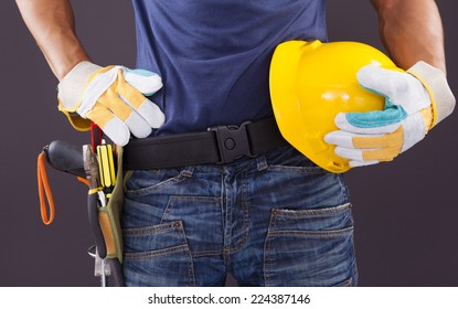 Close Up Of A Worker With Toolbelt And Helmet Against Black Background