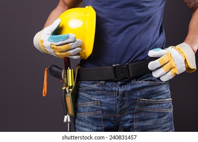 Close Up Of A Worker With Toolbelt And Helmet Against Black Background