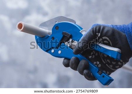 Close up of worker using pipe cutter to cut plastic PVC pipe during plumbing installation. Construction and repair concept suitable for building services, home renovation and professional tools