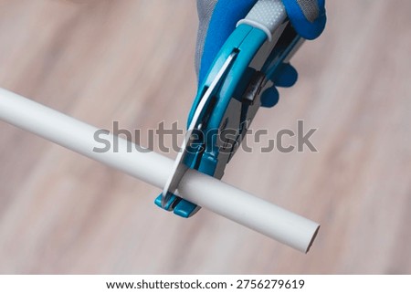 Close up of worker using pipe cutter to cut plastic PVC pipe during plumbing installation. Construction and repair concept suitable for building services, home renovation and professional tools