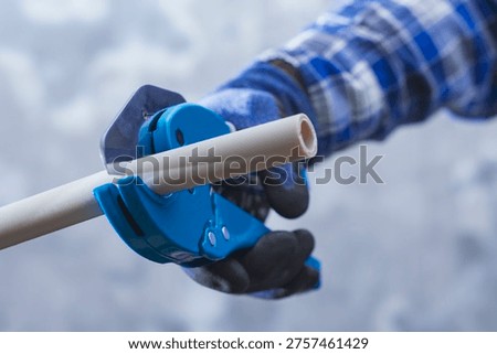 Close up of worker using pipe cutter to cut plastic PVC pipe during plumbing installation. Construction and repair concept suitable for building services, home renovation and professional tools