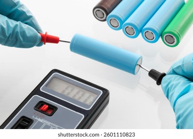 close up of worker's hand in gloves, using multimeter to check voltage on 18650 lithium-ion Battery Cells, on isolated white background