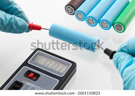 close up of worker's hand in gloves, using multimeter to check voltage on 18650 lithium-ion Battery Cells, on isolated white background