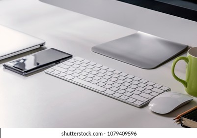 Close Up Working Place For Start Up Business With Desktop Computer, White Keyboard, Mouse, Smartphone And Laptop. 