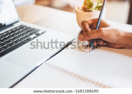 Close up of working woman hand using laptop computer and writing letter on notebook paper in office desk. Business and people lifestyles. Financial and Economy investment. Work from home concept