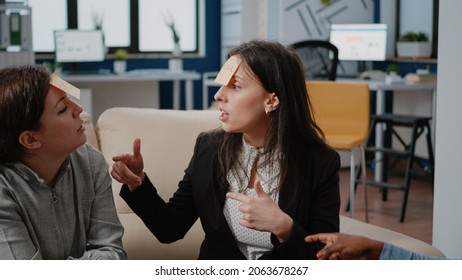 Close Up Of Workmates Enjoying Game To Guess With Sticky Notes To Do Fun Activity After Work. Colleagues Playing Charades, Celebrating Party With Drinks. Entertainment At Office.