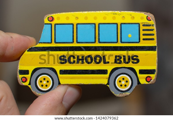 Close up of a worn toy yellow school bus\
puzzle piece with an adult hand.\
Conceptual.