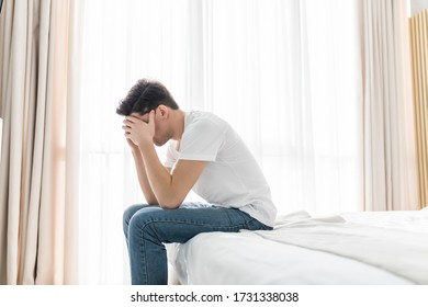 Close Up Of Worried Man Sitting On Bed With Hand On Forehead