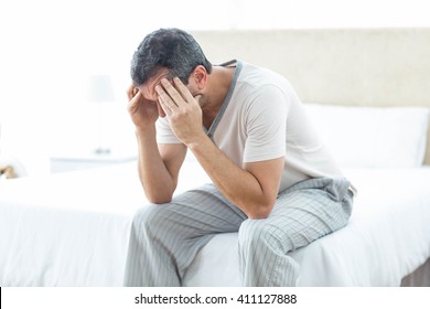 Close Up Of Worried Man Sitting On Bed With Hand On Forehead