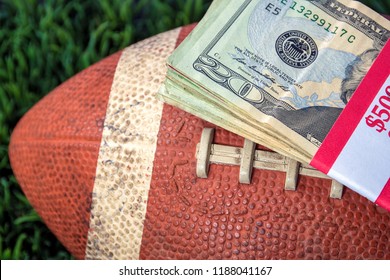 close up of wrapped money stack on used football and green grass background - Powered by Shutterstock