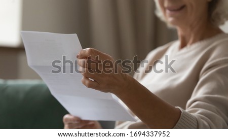 Close up wrinkled female hands holding paper document. Smiling happy middle aged senior woman reading letter, feeling excited by good news, final banking loan credit mortgage payment notification.