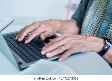 Close up of wrinkled hands typing on the laptop computer keyboard while working at home - Powered by Shutterstock