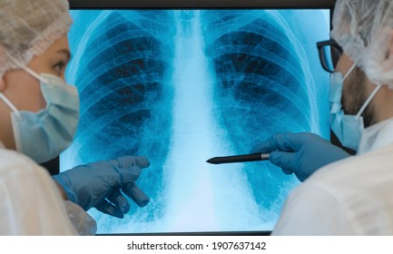 Close up of x-ray of patient with lung pneumonia caused by Coronavirus. Team of doctors at computer monitor in clinic discuss lungs are affected by virus. COVID-19