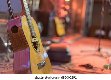 Close Up A Yellow Acoustic Guitar On A Stand In Front Of A Stage Set Up For An Upcoming Concert.