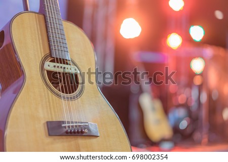 Close up yellow acoustic guitar on a stand in front of a stage set up for an upcoming concert.