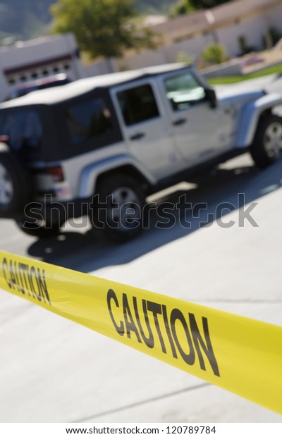 Close up of yellow caution tape with car in\
the background