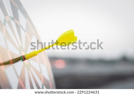 Close up yellow dart arrow hitting target center dartboard on sunset background. Business targeting and focus concept.