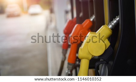 Close up yellow fuel nozzle with blurred 
 orange and red nozzle background at gas station service with sun light at sunny day.
