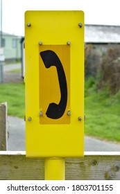 Close Up Of Yellow Rectangular Sign With Black Phone Receiver Silhouette Icon Outside By A Railway Line In Spring.  A Help Symbol Advisory Board On A Post
