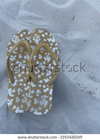 Close up of yellow thongs on the beach. Shoes have small white flowers on them. A woman’s flip flops.