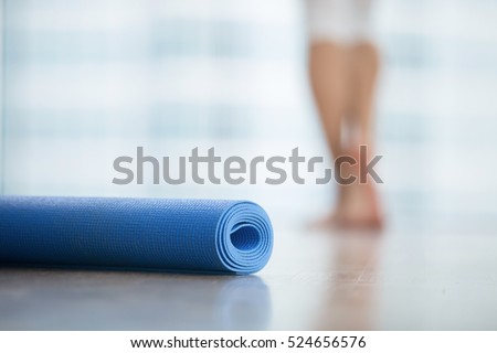 Close up of yoga, fitness, foam exercise mat fix in a roll in living room or fitness center, blurred female body at the background, resting after yoga, fitness class. Healthy lifestyle concept