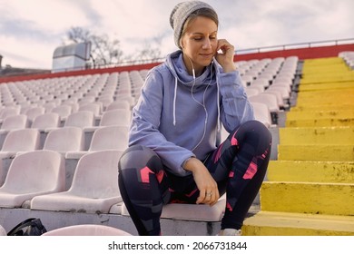 close up of young adult caucasian female sitting alone at the stadium, smiling, with headphones in her ears. handsfree cellphone conversation