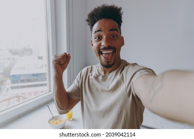 Close Up Young African American Man In Casual Clothes Do Winner Gesture Clench Fist Do Selfie Shot Pov On Mobile Phone Prepare Cooking Food In Light Kitchen At Home Alone Indoor Healthy Diet Concept.