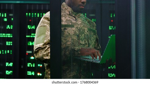 Close Up Of Young African American Military Officer Checking Work Of Servers In Analytic Monioring Center. Man With Laptop Computer Control Networking In Dark Room Cybersecurity In Army Concept.