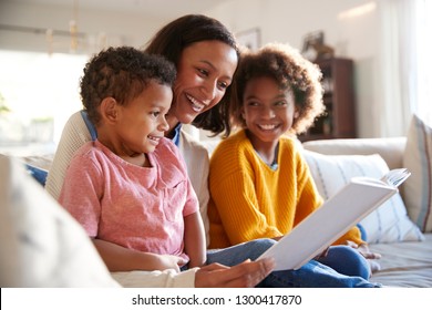 Close Up Of Young African American Mother Sitting On A Sofa In The Living Room Reading A Book To Her Two Children, Close Up, Side View