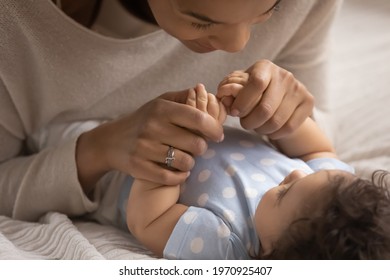 Close up of young African American mother cuddle play with little newborn baby girl child at home together. Happy ethnic mom enjoy motherhood with biracial toddler daughter kid. Parenthood concept.