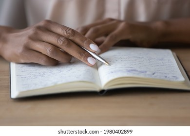 Close up young african american woman holding pen in hands, reading notes in copybook, repeating educational information preparing for exam. Focused mixed business lady managing assignments in planner - Powered by Shutterstock