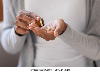 Close up young african ethnicity biracial woman pouring pills from bottle, taking daily dose of complex vitamins or prescribed medicine antibiotics, reducing painful feelings or strengthen immunity.