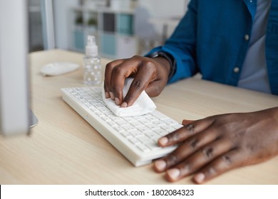 Close Up Of Young African-American Man Wiping Keyboard With Sanitizing Wipes While Working At Desk In Post Pandemic Office, Copy Space