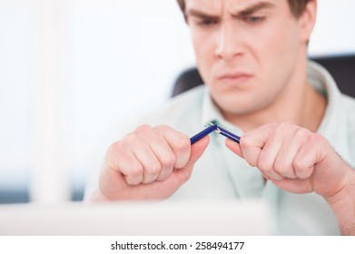 Close up of young angry businessman breaking blue pencil. Office interior with window - Powered by Shutterstock