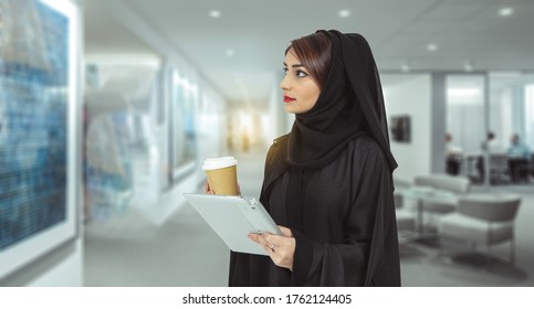 Close up of young Arabic business woman holding coffee and tablet,  looking at canvas on the wall in modern art gallery.