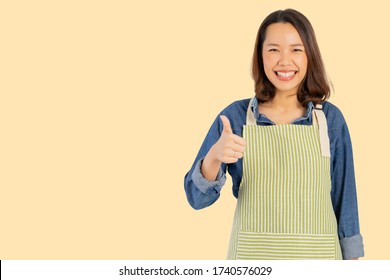 close up young asian adult woman (housewife) wear apron and raising hand thumb up for best score isolated on cream color background for good taste concept - Powered by Shutterstock