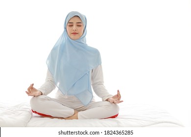 Close up young asian arab woman sitting on bed and enjoying meditation. Beautiful muslim in sleepwear with blue hijab practices yoga in bedroom with peace and calm. Healthy and lifestyle concept - Powered by Shutterstock