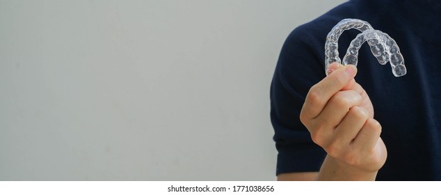 cerrar la mano de un joven asiático que sostiene un retenedor dental (invisible) en la clínica dental para el concepto de curso de tratamiento de dientes hermosos