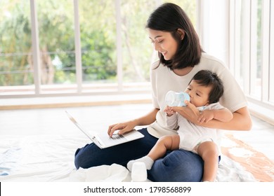 Close up of Young asian mother on maternity leave trying to freelance by the desk with toddler child.Stay at home mom working remotely on laptop while taking care of her baby.