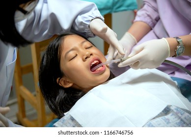 Close up of young Asian Pre teen girl having dental professional treatment in stomatology clinic. Kid patient at dental office open mouth with suction. Dentist examining and cleaning her teeth.