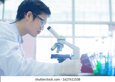 close up young asian scientist looking at microscope to research or record and analyze about scientific experiment result at laboratory for healthcare and pharmaceutical concept
