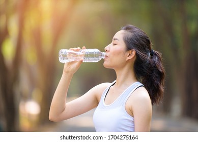 Close Up Young Asian Woman Drink Water From A Plastic Bottle After Do Sport In The Morning In A Park During Summer Day