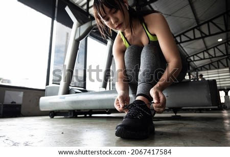 Close up of young asian woman lacing sports shoes before exercise at the gym.