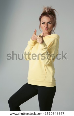 Close up of young attractive caucasian woman in yellow hoodies looking at camera posing funny, shocked with expression. Positive emotions of girl. Model tests on white background