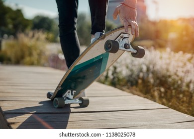Close up of young attractive man riding longboard in the park.