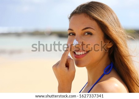 Close up young beautiful woman applying sun cream protection on her nose on the beach. Suntan lotion woman applying sunscreen solar cream.
