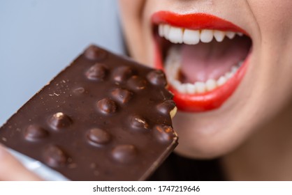 Close Up Of A Young Beautiful Woman Eating Chocolate. Cropped Photo. Closeup. Black Chocolate With Nuts.