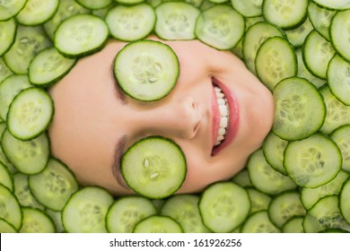 Close up of a young beautiful woman with facial mask of cucumber slices on her face at spa salon - Powered by Shutterstock